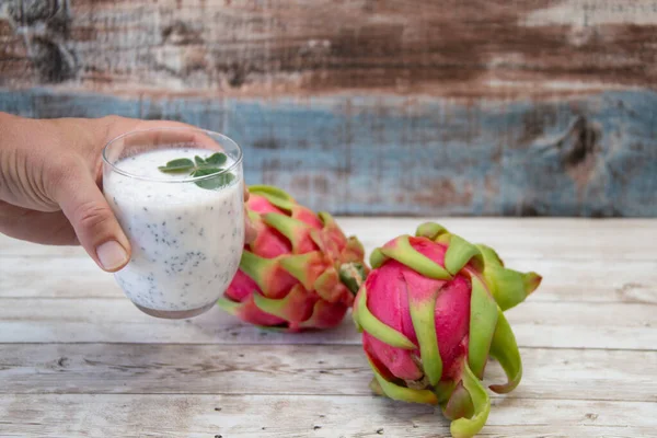 Elinde bir bardak beyaz chia tohumu smoothie ile naneli, kırsal ahşap pitaya yanında. Sağlıklı içecek konsepti