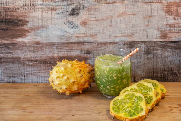 Kiwano kavunu, bütün ve dilimlenmiş, canlandırıcı bir meyve suyu ile, ahşap bir arka planda. Sağlıklı yaşam için egzotik meyve