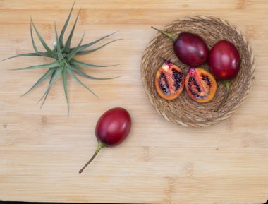 Taze tamarillo meyveleri, bütün ve dilimlenmiş, canlı kırmızı deri ve koyu kırmızı posa ile ahşap arka planda siyah tohumlar sergilenir.