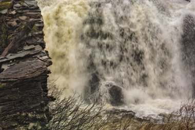 Karanlık bir kayanın üzerinde çağlayan kubbeli su vahşi ve evcilleştirilmemiş bir arazide doğanın ham gücünü gösteriyor.