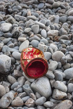 Çürümüş kırmızı boya kayalık çakıl taşlı plajda terk edilebilir. Kıyı şeridindeki kirliliği, kirliliği ve çevresel ihmali simgeler.