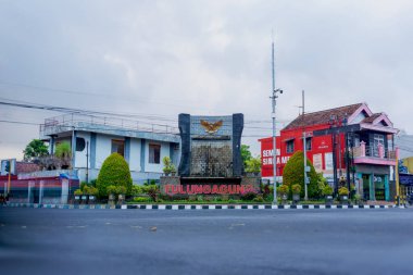 Tulungagung, Endonezya 'daki merkezi anıt, Garuda Pancasila amblemi ve şehir ismine sahiptir. Ticari binalar, siyasi reklam panoları ve öğleden sonra bulanık trafik hareketleriyle çevrili..