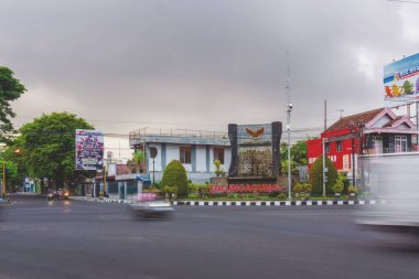 Tulungagung, Endonezya 'daki merkezi anıt, Garuda Pancasila amblemi ve şehir ismine sahiptir. Ticari binalar, siyasi reklam panoları ve öğleden sonra bulanık trafik hareketleriyle çevrili..