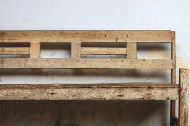 Basit, rustik ahşap bir bankın ya da sandalye çerçevesinin ön çekimi, aşırı yıpranmış ve yaşlanmış, kirli beyaz bir duvara yaslanmış, sarı su lekeleri ve soyulmuş boya ile. Yaş, bekleme veya ihmal kavramları için idealdir..