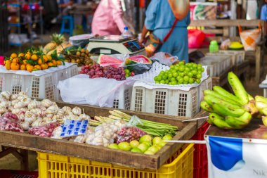 Sarımsak, yeşil ve kırmızı üzüm, portakal, limon otu ve muz gibi çeşitli taze sebze ve meyveler kalabalık bir Asya pazarında ahşap bir tezgahta üst üste yığıldı..
