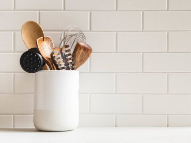 Beyaz mutfak arka planı, beyaz tezgahta seramik kavanozda mutfak aletleri, metin için kopyalama alanı, ön görünüm