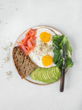 Beyaz tabakta kızarmış yumurta, avokado, ekmek ve hafif bir arka planda marul. Üst Manzara. Boşluğu kopyala