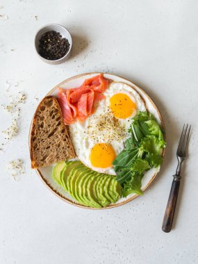 Beyaz tabakta kızarmış yumurta, avokado, ekmek ve hafif bir arka planda marul. Üst Manzara. Boşluğu kopyala