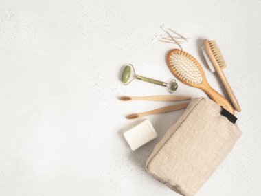 Kadınlar için bakım ve hijyen malzemeleriyle dolu bir eko kozmetik çantası. Bambu diş fırçası, tarak, kristal masaj aleti, sünger taşı fırçası, pamuk çubukları ve gri arka planda sabun. Düz yatıyordu. kopyalama alanı. en üstteki görünüm.