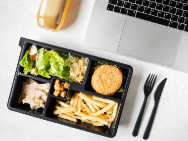 Pakette sezar salatası, hamburger ve patates kızartması olan öğle yemeği paketi paket servis edilecek veya yemek servisi ve dizüstü bilgisayar. Yemek teslimatı konsepti. Üst Manzara. Boşluğu kopyala