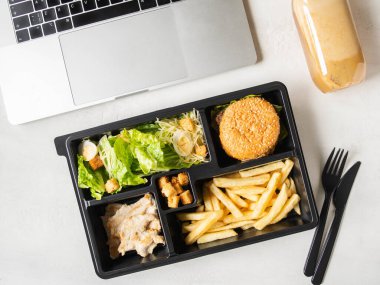 Pakette sezar salatası, hamburger ve patates kızartması olan öğle yemeği paketi paket servis edilecek veya yemek servisi ve dizüstü bilgisayar. Yemek teslimatı konsepti. Üst Manzara. Boşluğu kopyala