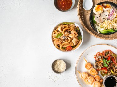 Asya yemeği hazırla - ramen çorbası, ızgara karides, kızartma sebzesi ve beyaz arka planda deniz ürünleri ile udon. Üst Manzara. Uzayı kopyala Düz yatıyordu