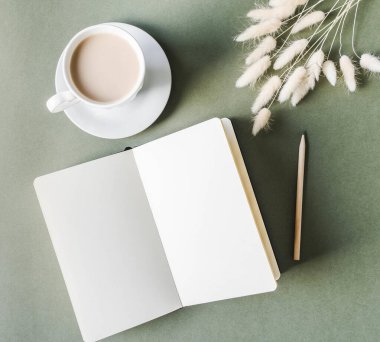 Boş çarşaflı defteri aç, yeşil arka planda kahve bardağı olsun. Üst görünüm.