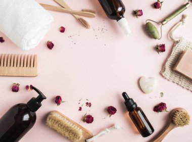 Çeşitli kozmetik ürünlerinden çerçeveler, ahşap fırçalar, taraklar ve pembe arka plandaki kuru güller. Üst Manzara. Boşluğu kopyala