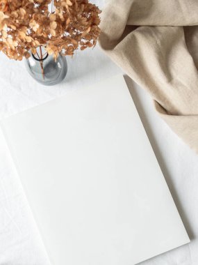 Boş boş beyaz dergi kapağı, arka planda kurumuş çiçekli vazo ve maket yap. Düz yatıyordu. Üst Manzara. Boşluğu kopyala