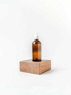 Ahşap küp kürsünün üzerinde cam kahverengi kozmetik şişeyle beyaz arka plan manzarası. İzole edilmiş kozmetik konsepti.