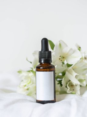 Beyaz kepekli kozmetik kehribar cam şişe ve beyaz arka planda beyaz çiçekler. Spa, güzellik salonu, blog yazarlığı ve reklamcılık için yaratıcı bir konsept..