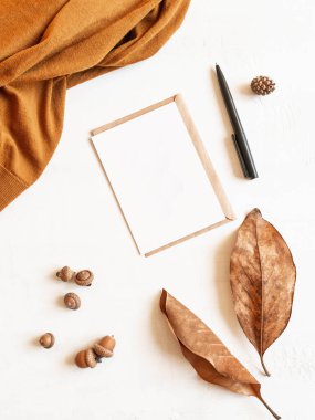 Kahverengi süveter, güz yaprağı ve meşe palamudu çerçevesi, beyaz arka planda zarf ve kartpostal. Üst Manzara. kopyalama alanı. En düşük sonbahar bileşimi