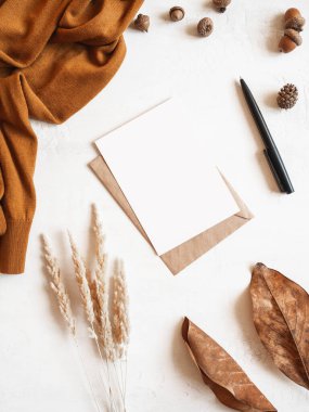 Kahverengi süveter, kuru çimen, sonbahar yaprağı ve meşe palamudu, zarf ve beyaz arka planda kartpostal çerçevesi. Üst Manzara. kopyalama alanı. En düşük sonbahar bileşimi