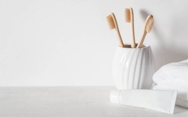 Seramik camlı bambu diş fırçaları, beyaz diş macunu tüpü ve beyaz havlularla minimum banyo arkaplanı. Ön manzara. Boşluğu kopyala