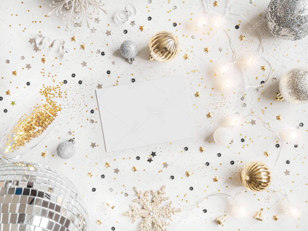 Flat lay of Christmas or New year party disco ball, garland, season decoration and empty white postcard on white background. Holiday and invitation mockup. Christmas or new year wish layout. Copy space. Top view
