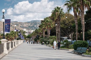 Reggio Calabria, İtalya 30 Eylül 2025: Lungomare Falcomata gezinti alanı boyunca yürüyen insanlar, güney İtalya 'da popüler bir sahil kamusal alanı olan palmiye ağaçları ile dolular..