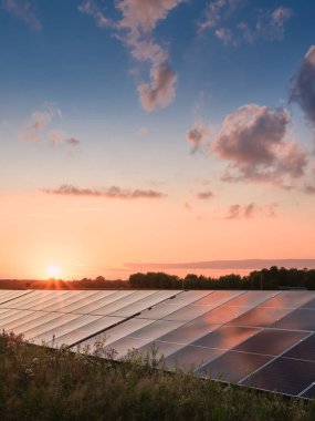 Günbatımında güneş paneli çiftliği renkli gökyüzünün altındaki yansıtıcı panellerle yenilenebilir ve sürdürülebilir temiz enerjiyi sembolize ediyor..