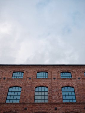Kemerli pencereli tuğla bina cephesi ve bulutlu gökyüzü, metin ve tasarım kullanımı için kopyalama alanı olan endüstriyel mimari arkaplan.