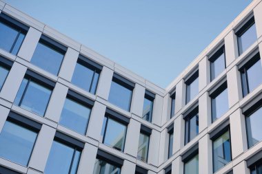 Cam pencereli modern ofis binası cephesi ve temiz mavi gökyüzüne karşı metal paneller, kurumsal arkaplan için temiz geometrik mimari.