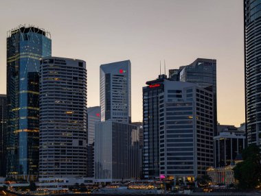 Brisbane, Queensland, Avustralya - 6 Aralık 2025: Brisbane merkez ticaret bölgesindeki modern ofis kulelerinin akşam manzarası Deloitte, JLL ve BDO logoları şehrin ışıkları alacakaranlıkta yanarken aydınlandı.