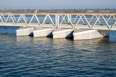 Üzerinde dört tekne olan bir köprü. Su sakin ve gökyüzü mavi. Köprü metalden yapılmıştır ve bir su kütlesinin üzerindedir. Villeneuve-les-Maguelone 'da, Fransa' nın güneyinde Herault Bölümü 'nde bir kasaba.