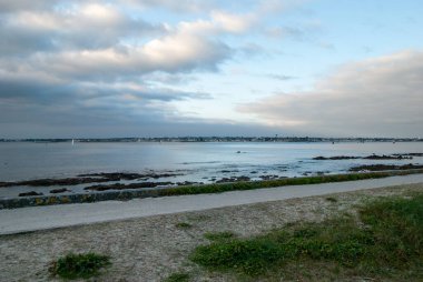Arka planda bulutlu bir gökyüzü olan bir plaj. Su sakin ve sahil kayalarla kaplı. Gavres Yarımadası, Britanya, Fransa