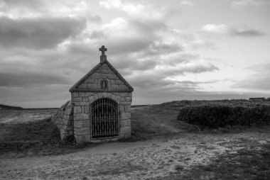 Üzerinde haç olan küçük bir taş bina. Binanın etrafı tarlalarla çevrili ve terk edilmiş. Gavres Yarımadası, Britanya, Fransa