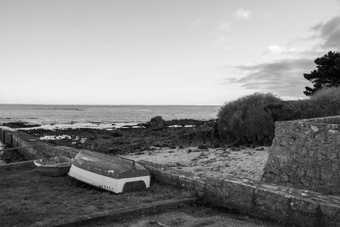 Sahilde bir duvarın yanında bir tekne oturuyor. Gökyüzü bulutlu ve su sakin. Gavres Yarımadası, Britanya, Fransa