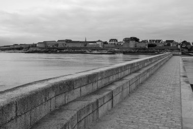 Taştan bir duvarı ve ona giden basamakları olan bir rıhtımın siyah beyaz fotoğrafı. Rıhtım bir su kütlesinin yanında ve arka planda birkaç ev var. Gavres Yarımadası, Britanya, Fransa