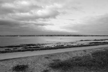 Arka planda bulutlu bir gökyüzü olan bir plaj. Su sakin ve sahil boş. Gavres Yarımadası, Britanya, Fransa