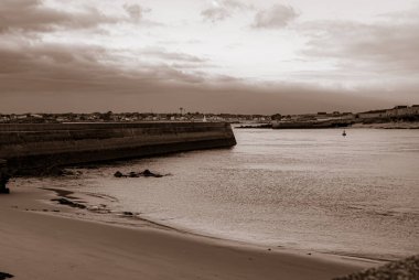 Limanı ve teknesi olan bir sahil. Gökyüzü bulutlu ve su sakin. Gavres Yarımadası, Britanya, Fransa