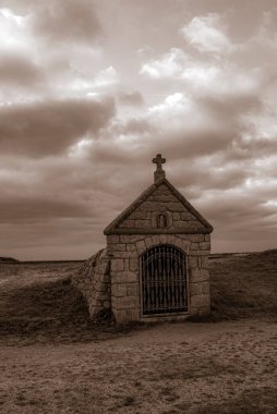 Üzerinde haç olan küçük bir taş bina. Bina bir toprak tarlasıyla çevrili. Gavres Yarımadası, Britanya, Fransa