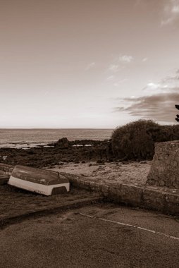 Sahilde bir duvarın yanında bir tekne oturuyor. Gökyüzü bulutlu ve su sakin. Gavres Yarımadası, Britanya, Fransa