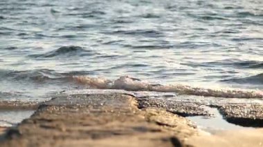 4K yakın çekim videosu günbatımında beton bir levha veya kaya üzerinde hafif dalga hareketlerini gösteriyor. Su dokusuna, altın saat ışığına ve düşük açılı perspektife odaklan..
