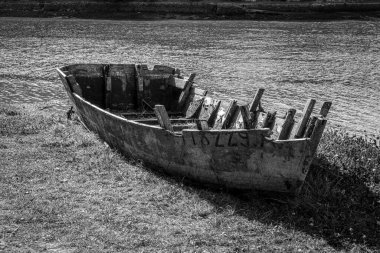 Nehrin kenarındaki çimlerin üzerinde bir tekne oturuyor. Tekne eski ve üzerinde 