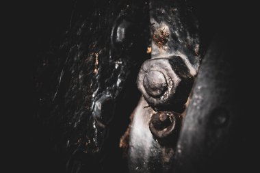 Siyah arka planı olan paslı bir sürgüye yakın çekim. Cıvata diğer paslı cıvatalarla çevrili ve yıpranmış görünüyor.