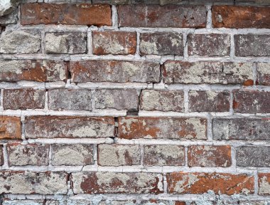 Kırmızımsı kahverengi tuğlalar ve parçalanmış gri harç ve alçı parçalarının karışımından oluşan eskimiş ve yıpranmış bir tuğla duvar, desenli ve tarihsel karakterini vurguluyor..