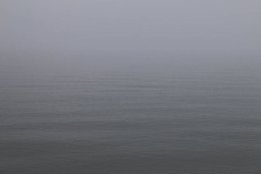 Yoğun sis altında geniş ve sakin bir su. Ufuk zar zor görülüyor. Yumuşak, sessiz tonlar ve hafif dalgalarla minimalist ve sakin bir sahne yaratıyor. Huzurlu, iç gözlemci atmosfer.