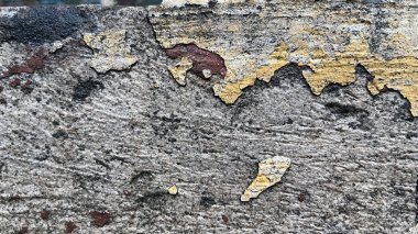 Sarı ve kırmızı boyalı eskimiş beton duvarın yakın çekimi pürüzlü yüzeyi, yaş ve çürüme izlerini ortaya çıkarıyor..