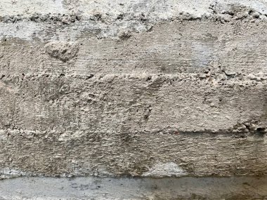 Kaba beton bir yüzeye yakın çekim, görünür çizgiler ve ahşap kalıplardan çıkıntılar, gri tonlarda gösterilen doku ve inşaat ayrıntıları..