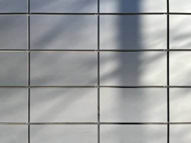 Sunlight casts soft shadows on a grid of smooth, light gray tiles, creating a minimalist, geometric pattern with a clean, modern aesthetic.