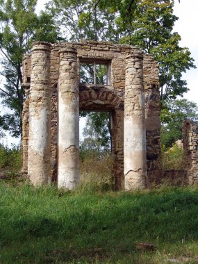 Yıpranmış dört sütun ve yemyeşil ve uzun ağaçlarla çevrili kemerli antik taş kalıntıları. Zamansız mimari ve doğal çürümeyi çağrıştıran tarihi bir yer..