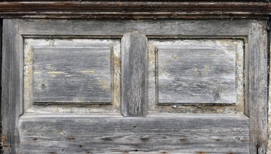 Yıpranmış ahşap bir panele yakın çekim, iki dikdörtgen kesitli ve merkezi dikey şeritli, eski gri boya, çatlaklar ve kabuk soyma dokusunu gösteriyor..