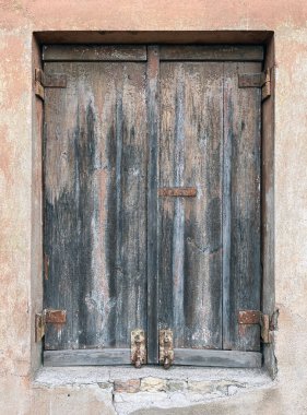 Eski ahşap panjurlar yıpranmış, çatlamış yüzey ve paslı metal menteşeler görünür hasarla solmuş alçı bir duvar ve kırsal, antika bir görünüm için boya soyuyorlar..